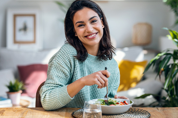 A woman in a teal sweater smiling and eating lunch.