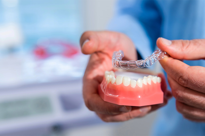 Dentist placing clear aligner on model of teeth.