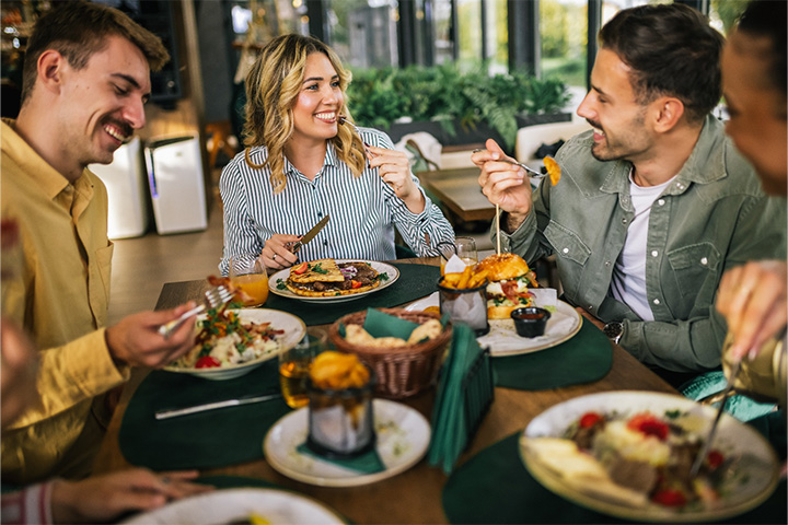 Group of friends smiling while eating meal together at restaurant.