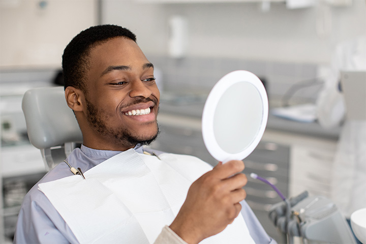 Man smiling at reflection in handheld mirror.