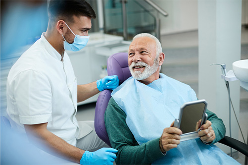 Senior patient looking at dentist while holding small mirror.
