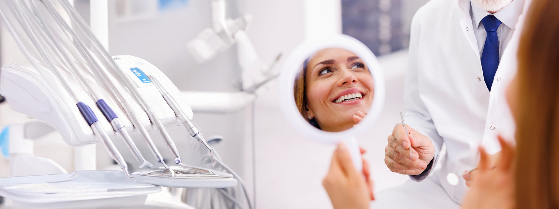 A woman looking at her teeth in a handheld mirror in a dental office.