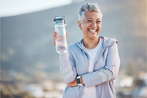 Woman smiling with water bottle on hike outside.